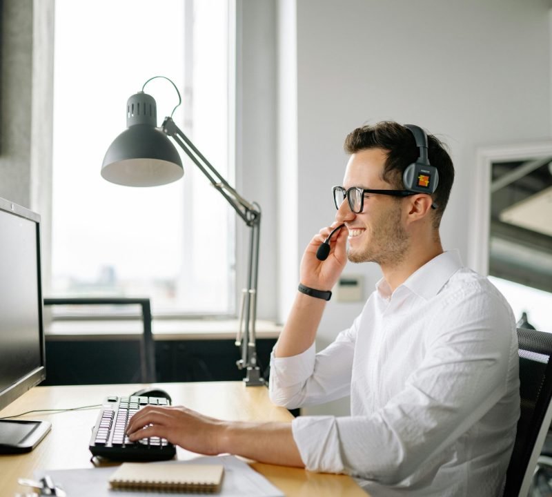 Smiling man wearing headset working at computer in bright office.